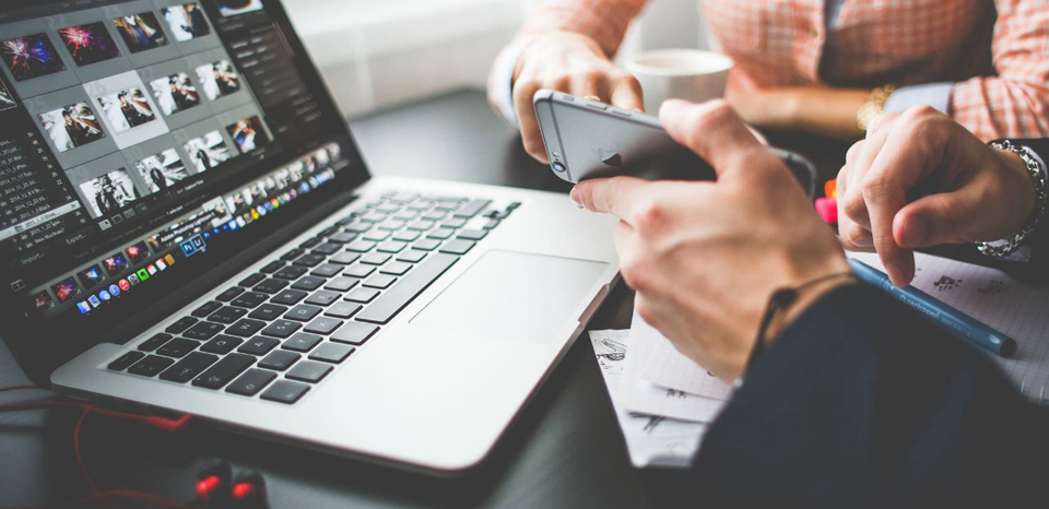 Las manos de dos personas donde una sujeta un móvil y parecen hablar de su contenido