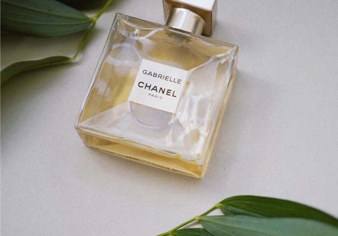 Image of a Gabrielle Essence perfume bottle along with some green leaves.